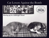 Calendar cover with two cats resting on a plaid blanket and a quilt, featuring the text 'Resting up for challenges ahead' and '2026'.
